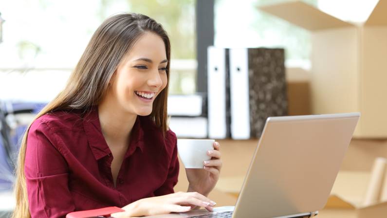 Beautiful female worker working on line with a laptop during office relocation with carton boxes in the background